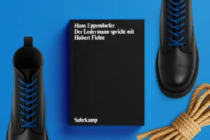 Zu sehen ist: das Buch Der Ledermann spricht mit Hubert Fichte, umgeben von Springerstiefeln und einem Seil.