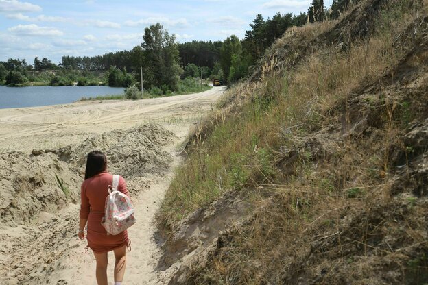 Eine Frau von hinten, die auf einem Sandweg an einem Grashügel entlang geht