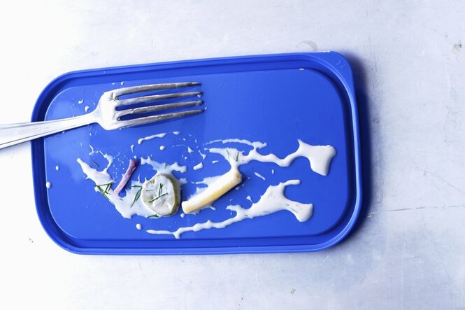 Blauer Deckel eines Plastikbehälter, darauf Spuren von Nudelsalat und eine Gabel