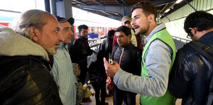 Flüchtlinge sprechen mit einem Helfer in grüner Weste