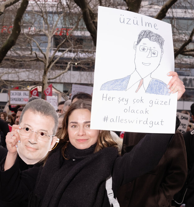 Eine Frau hält eine Kinderzeichnung mit einem Porträt von Imamoglu und einer Maske von seinem Gesicht