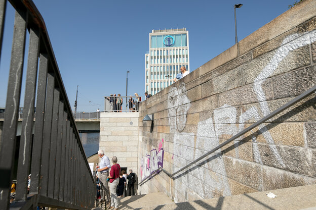 Menschen stehen an einer Treppe an einer Kaimauer, dahinter ragt ein Gebäude mit dem Firmenlogo von Kühne+Nagel auf