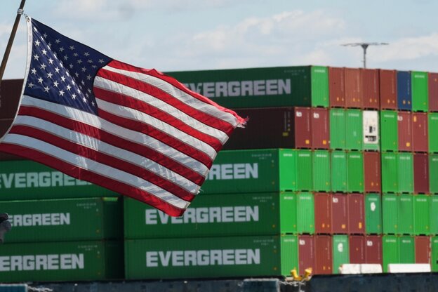 Container sind im Hafen von Los Angeles gestapelt während im Vordergrund eine US-Flagge weht.