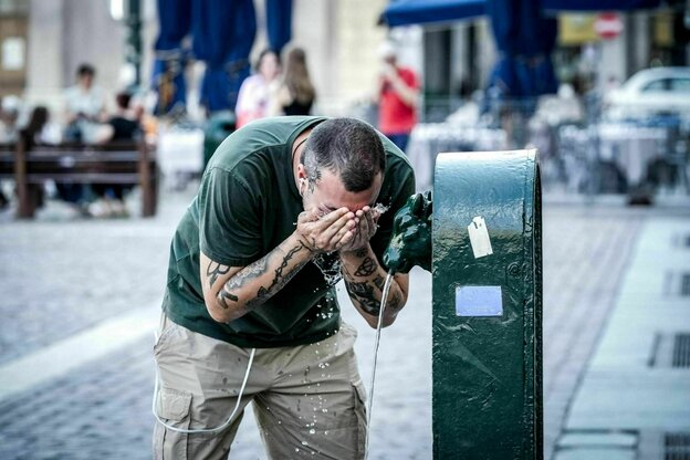 Sommer in der Stadt - ein Mann mit tätowierten Unterarmen kühlt sein Gesicht mit Wasser an einem Brunnen