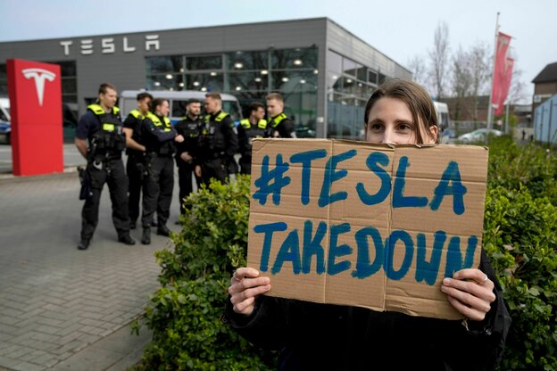 Protest mit Schild vor einer Tesla Filiale.