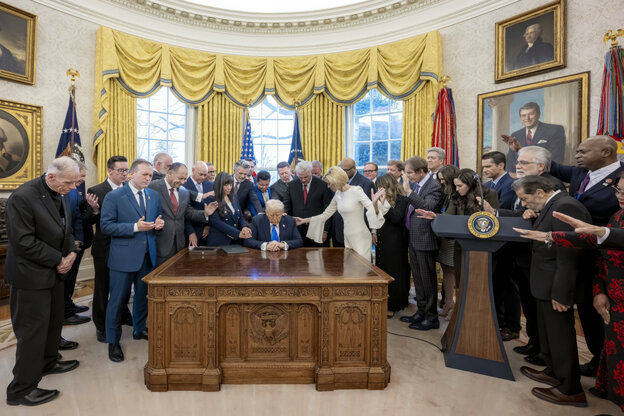 Donald Trump sitzt mit gebeugtem Kopf hinter dem Schreibtisch des Oval Office, er ist von Menschen umringt, deren Hände ihn zu segnen scheinen