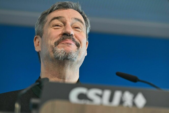 Ein Mann (Markus Söder) steht an einem Rednerpult und grinst süffisant