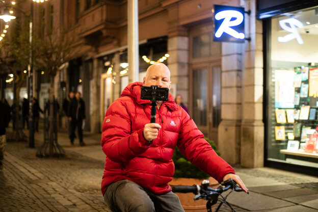 Stefan Bauer fährt mit roter Jacke auf einem Fahrrad, vor sich hält er eine Videokamera