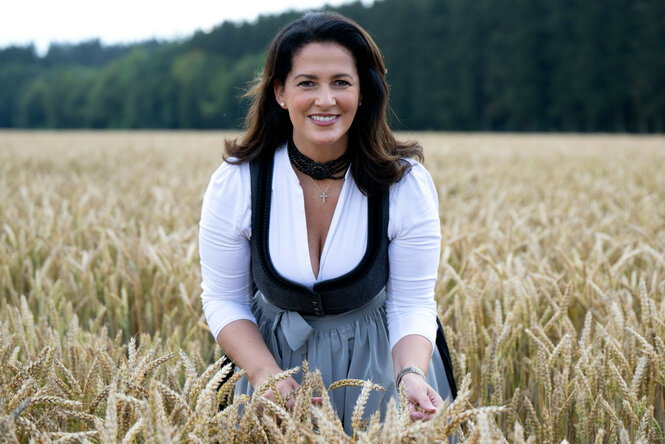 Zu sehen ist Michaela Kaniber, CSU-Politikerin und Kandidatin für das Bundeslandwirtschaftsministerium. Sie steht in einer traditionell anmutenden Tracht in einem Getreidefeld.