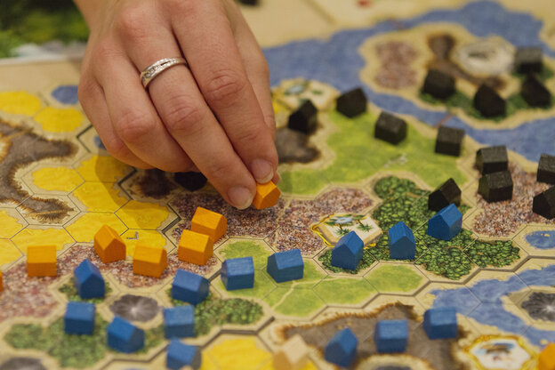 Eine Hand setzt Spielsteine auf einem Spielplan