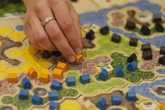 Eine Hand setzt Spielsteine auf einem Spielplan