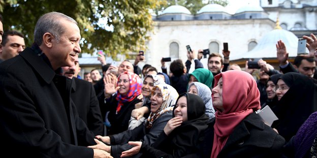 Links ein Mann mit grauen Haaren, der türkische Präsident Erdogan, rechts von ihm mehrere Frauen mit Kopftuch, die ihn anhimmeln