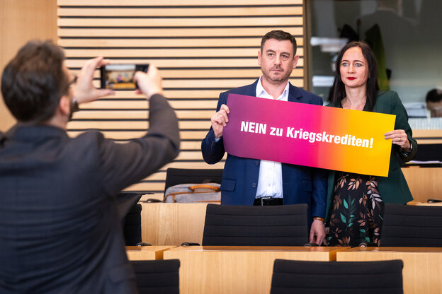 Sven Küntzel und Anke Wirsing stehen in einem Plenarsaal und lassen sich fotografieren, während sie gemeinsam ein Schild halten, auf dem steht: 