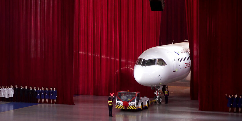 Die Nase eines Flugzeugs guckt – wie in einem Theatersaal – aus einem roten Vorhang hervor.