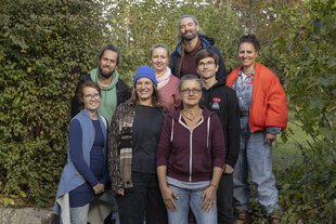 Gruppenfoto von acht Personen, die lächelnd in die Kamera blicken