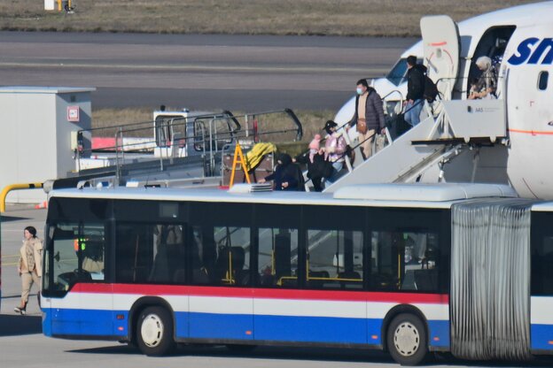 Aus der Ferne sehen wir, wie Passagiere aus einem Flugzeug in einen Bus steigen