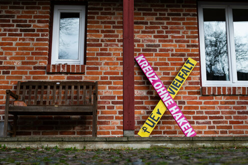 Vor einem Haus lehnt ein pink-gelbes Holzkreuz mit der Aufschrift "Kreuz ohne Haken - fUEr Vielfalt"