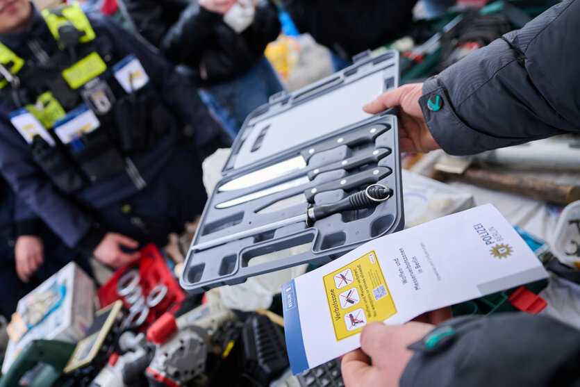 Ein Marktstandbesitzer fragt die Polizei, ob er weiterhin Küchenmesser verkaufen darf, während die Beamten Flyer in unterschiedlichen Sprachen auf dem Leopoldplatz verteilen