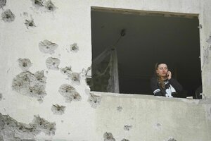 Eine Frau blickt aus dem Fenster eines zerschossenen Wohnhauses in Charkiw