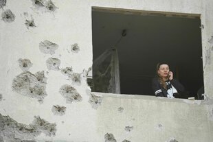 Eine Frau blickt aus dem Fenster eines zerschossenen Wohnhauses in Charkiw