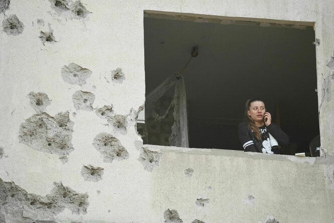 Eine Frau blickt aus dem Fenster eines zerschossenen Wohnhauses in Charkiw