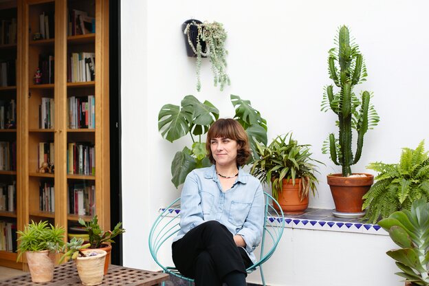 Eine Frau sitzt auf einem Balkon oder eine Terrasse vor Kakteen und Pflanzen