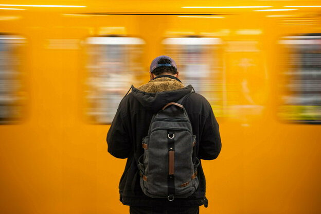 Ein Mann steht am Gleis eines U-Bahnhofs, während eine Bahn an ihm vorbeifährt.