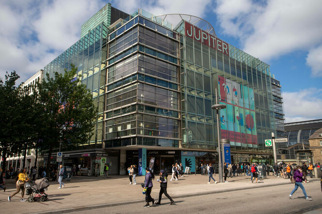 An einem großen Gebäude am Hamburger Hauptbahnhof laufen Menschen vorbei, auf dem Gebäude steht "Jupiter".