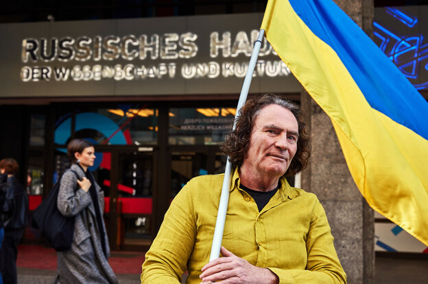 Ein Mann steht mit gelbem T-Shirt und ukrainischer Flagge vor dem Russischen Haus
