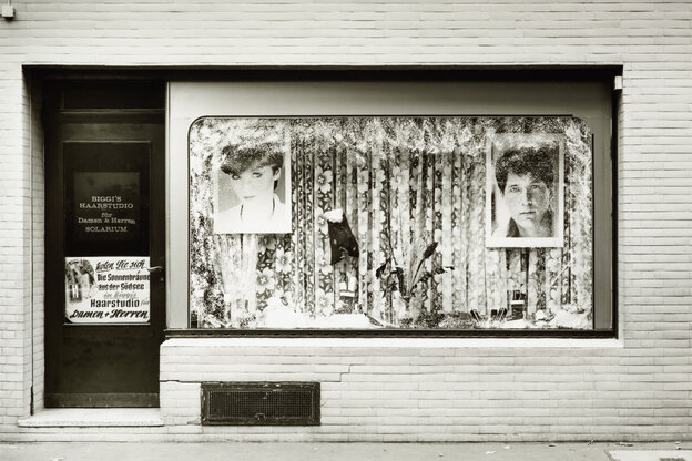 Sicht auf das Schaufenster eines Friseurladens in Köln 1980 mit den verblassten Fotografien von Frisurmodels vor zugezogenen Gardinen