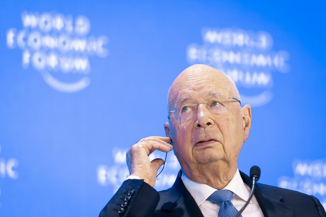 Klaus Schwab hält sich die Hand ans rechte Ohr, um besser aus einem Kopfhörer darin zu hören.