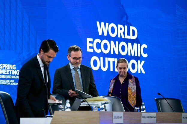 Zwei Männer und eine Frau ordnen ihre Unterlagen. Sie stehen vor einer blauen Wand mit dem Schriftzug: World Economic Outlook