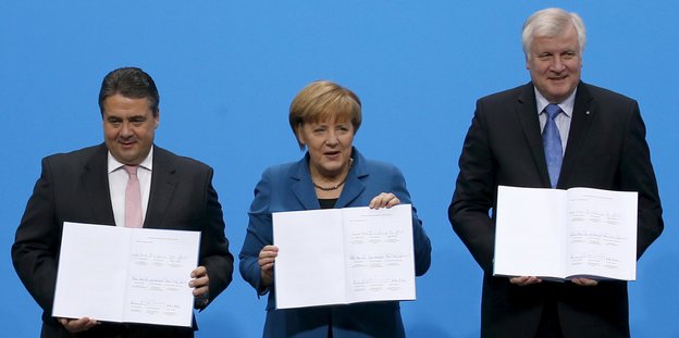 Sigmar Gabriel, Angela Merkel und Horst Seehofer stehen da und halten geöffnete Bücher hin - den Koalitionsvertrag