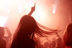 Eine Person mit langen Haaren tanzt in rötlichem Licht in einem Club, sie hebt einen Arm