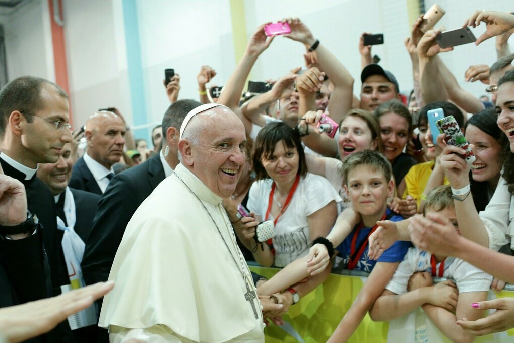 Papst Franziskus steht lächelnd vor einigen Menschen