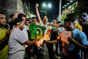 Mit hochgestreckter Faust hält ein Mann eine brennende pakistanische Flagge