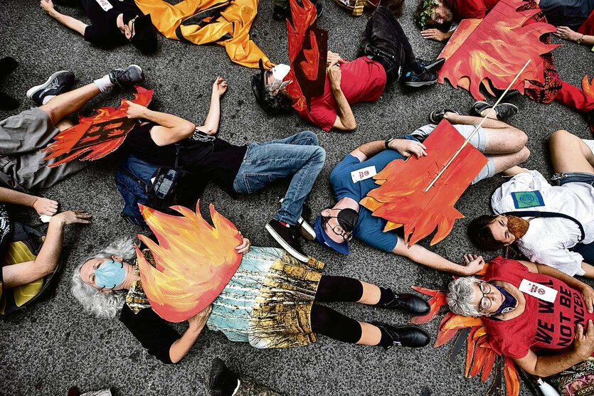 Klimaprotest in Gemeinschaft: Menschen liegen zusammen auf einer Straße und halten Schilder in die Luft, die wie Flammen aussehen