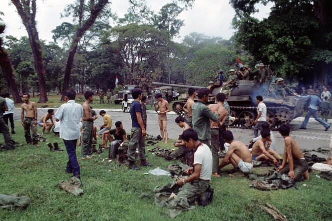 Saigon, 30. April 1975: Südvietnamesische Soldaten legen ihre Uniformen ab, während ein Panzer der nordvietnamesischen Armee vorbeifährt