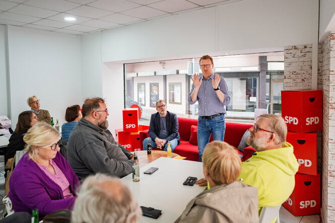 Der Bundestagsabgeordnete Oliver Kaczmarek steht , eine Gruppe hört ihm zu, rote SPD Würfel liegen im Raum