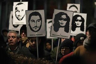 Demonstranten halten Plakate mit stilisierten Bildern der Opfer bei einem Gedenken zum Jahrestag des rassistischen Anschlages von Hanau am damaligen Tatort in Kesselstadt