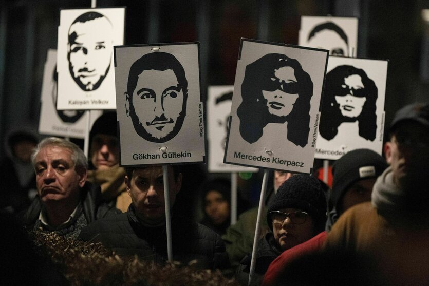 Demonstranten halten Plakate mit stilisierten Bildern der Opfer bei einem Gedenken zum Jahrestag des rassistischen Anschlages von Hanau am damaligen Tatort in Kesselstadt