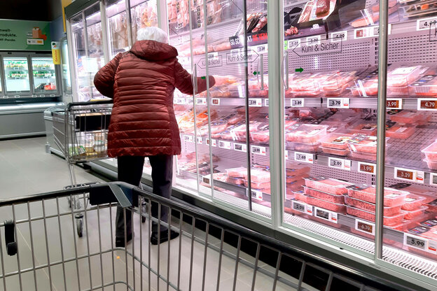 Ein ältere Frau nimmt abgepacktes Fleisch aus einem großen Kühlregal