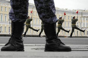 Vier russische Soldaten marschieren mit langgestreckten Beinen und roten Flaggen auf ihrem Bajonett - im Vordergrund sieht man die Steifel und Beine eines Soldaten
