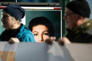 Zwei Teilnehmer einer Aktion stehen vor einem Wagen mit einem Bild von Sahra Wagenknecht