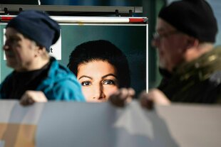 Zwei Teilnehmer einer Aktion stehen vor einem Wagen mit einem Bild von Sahra Wagenknecht