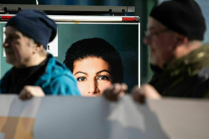 Zwei Teilnehmer einer Aktion stehen vor einem Wagen mit einem Bild von Sahra Wagenknecht