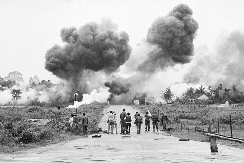 Journalisten beobachten aus der Entfernung die Bombardierung eines Dorfes im Vietnamkrieg