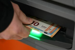 Ein Mann zieht Geldscheine aus dem Ausgabefach eines Geldautomaten