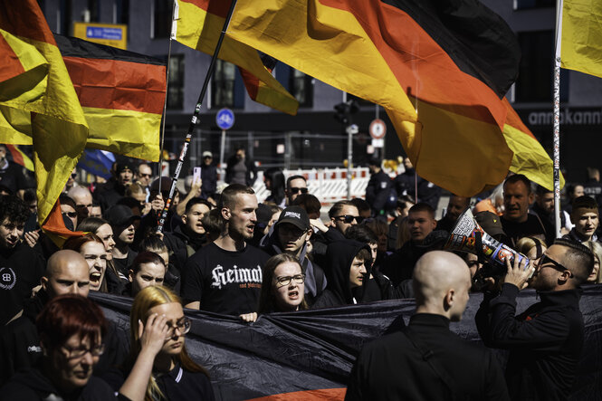 Deutschlandflaggen werden geschwenkt, die Teilnehmer tragen schwarze T-Shirts, auf einem steht "Heimat"
