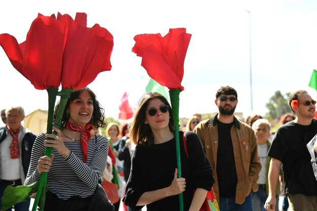 Zwei junge Frauen halten große Papier-Blumen mit roten Blüten in der Hand